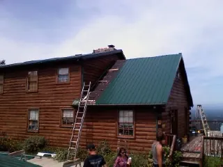 Green metal roof going on a two story log home with ladders set in Deerfield