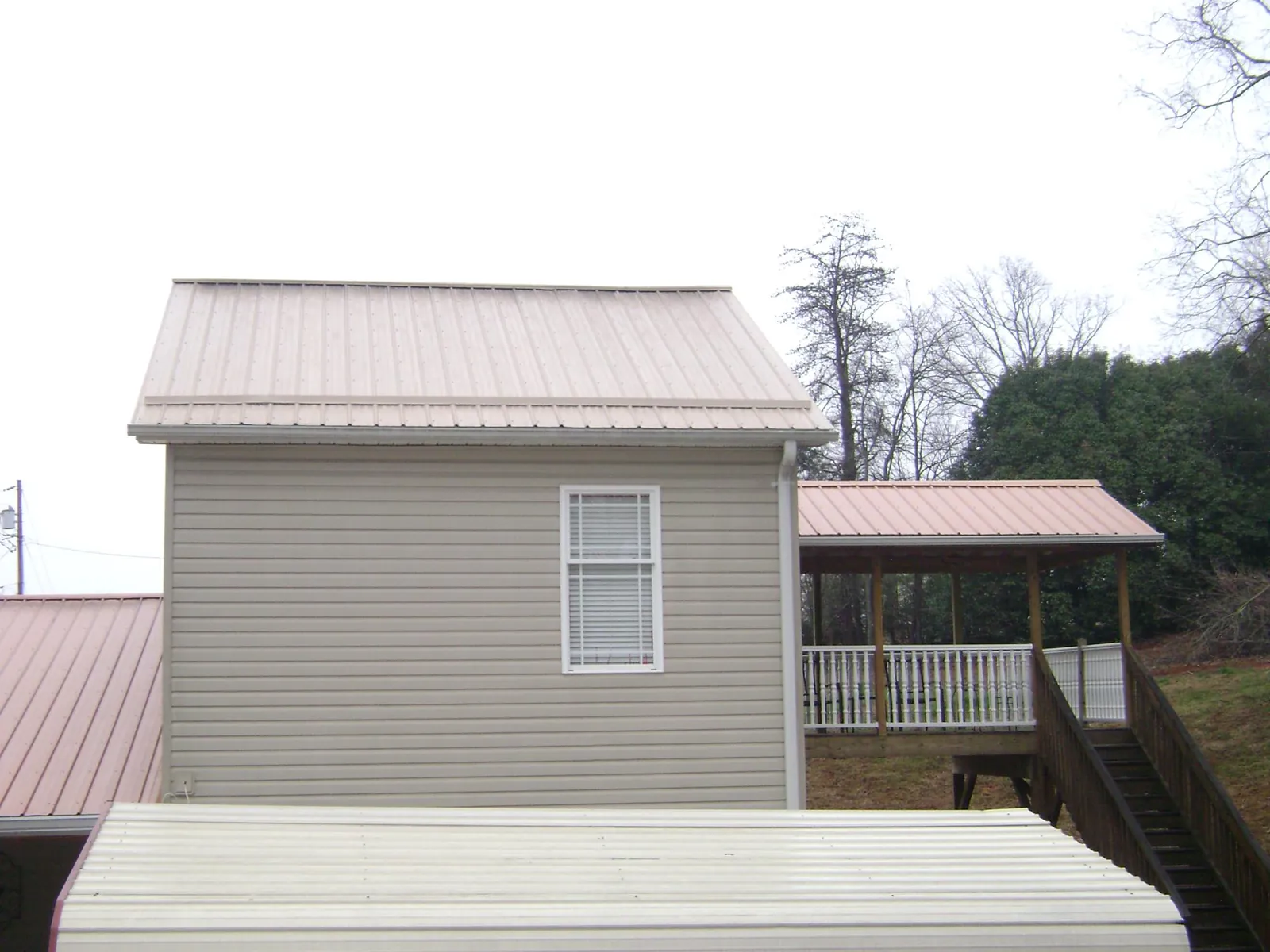 Tan metal roofs on a two story addition and attached porch, from a Roof Replacement job in Deerfield